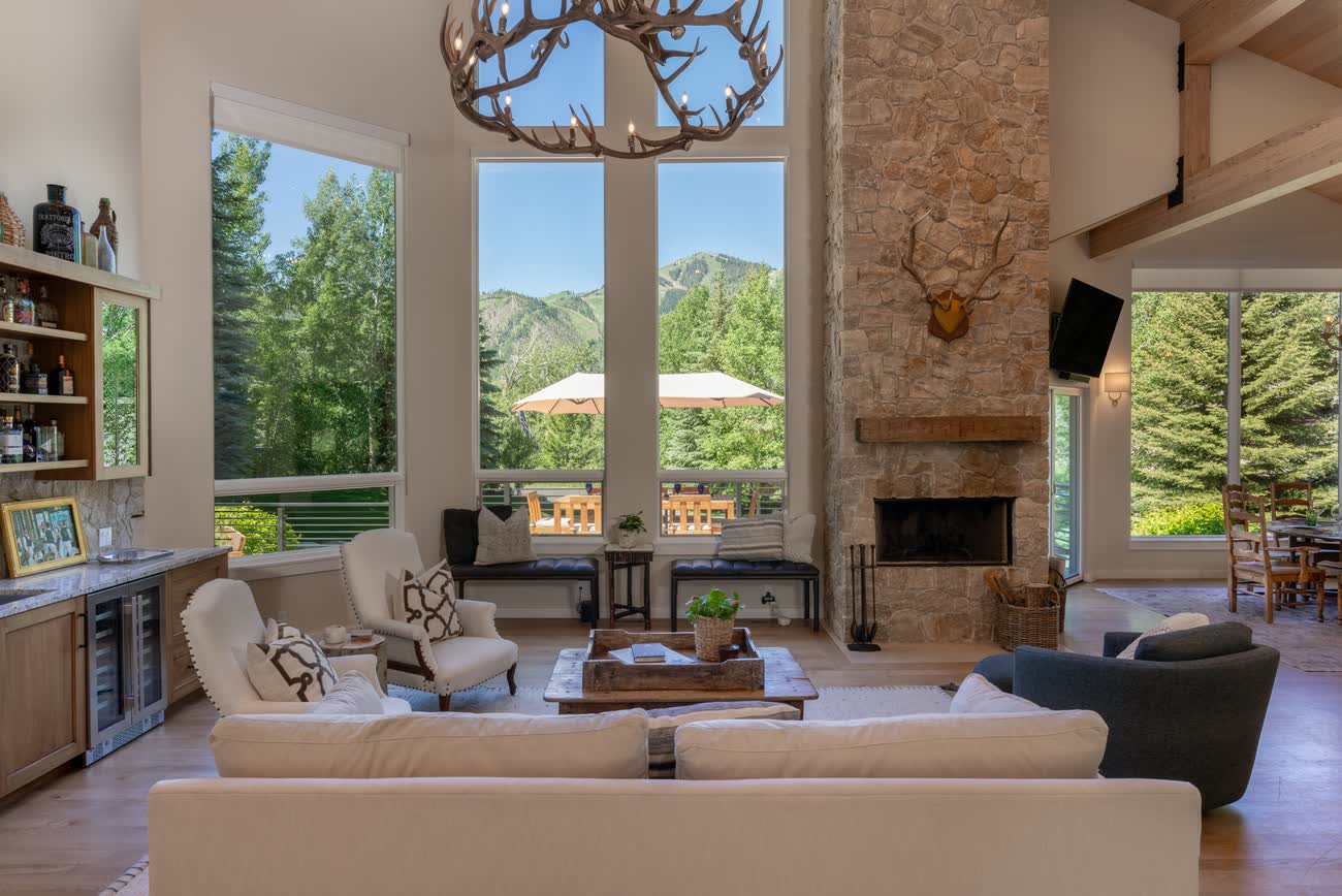 Great room with stone fireplace beneath full-height glass and timber beams