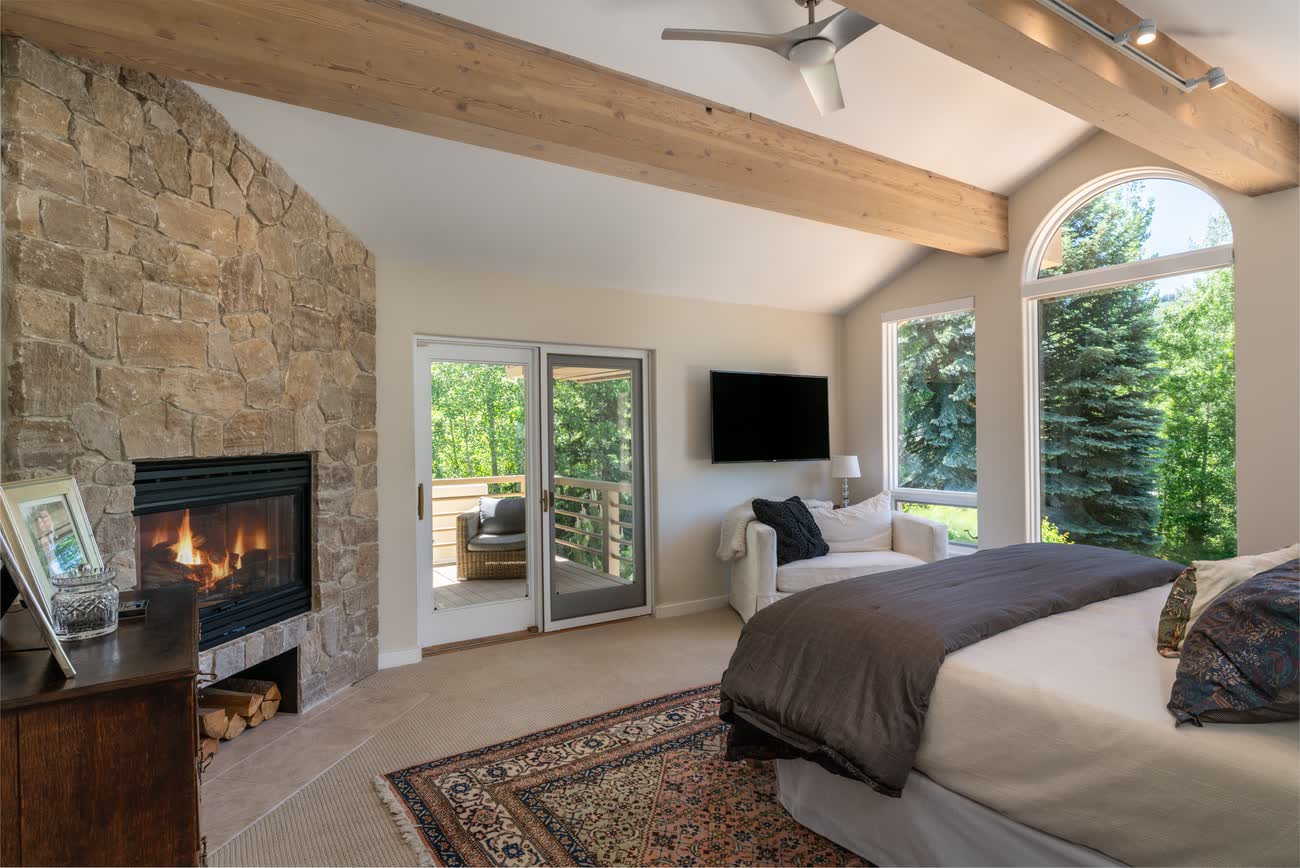 Primary bedroom with stone fireplace and arched windows to the hillside