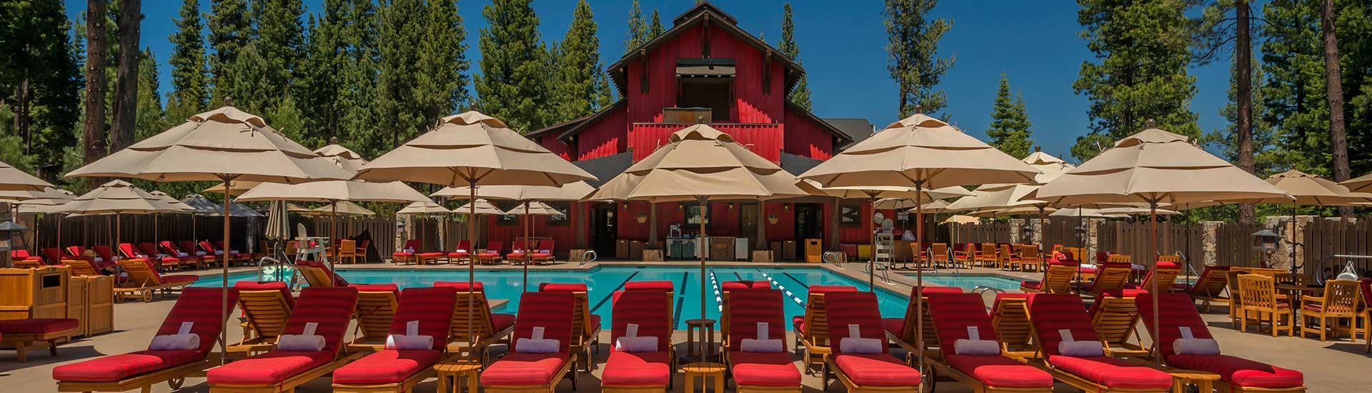 Martis Camp Family Barn pool with red loungers, market umbrellas, and Sierra Nevada pine trees in background