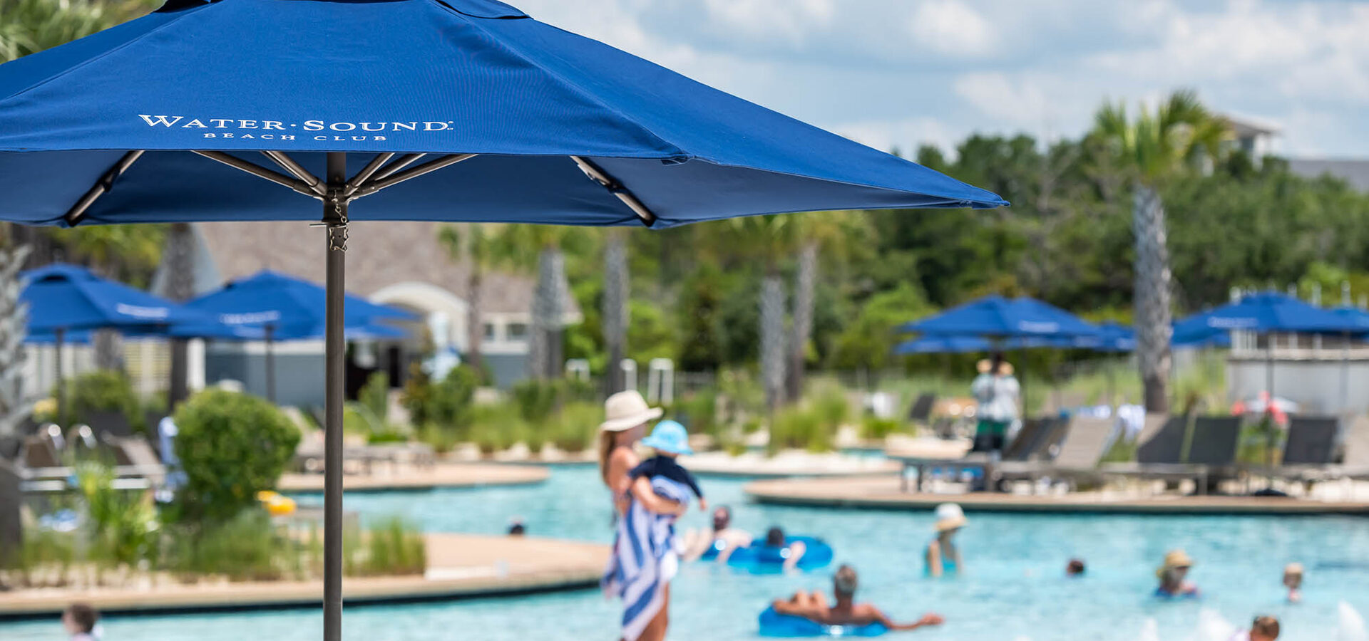 Watersound Club pool with branded blue umbrellas, members floating in lazy river on a sunny day